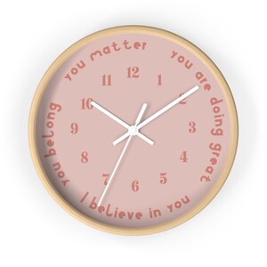 May include: A pink clock with a wooden frame and white hands. The clock face has the words "you matter", "you are doing great", and "I believe in you" written around the numbers.