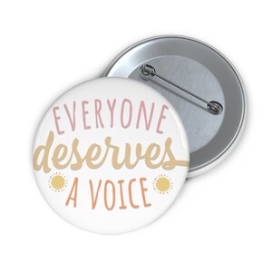 May include: A white button with a pink and yellow design. The button says "Everyone deserves a voice" with two yellow suns on either side of the text.