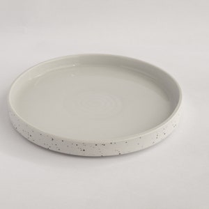May include: A white ceramic serving tray with a speckled grey rim. The tray is round and has a smooth, glossy finish.