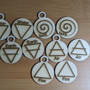 Könnte beinhalten: Eine Sammlung hölzerner Elementsymbole, darunter Wasser, Erde, Luft, Feuer und Geist. Jedes Symbol ist auf einer runden Holzscheibe mit einem kleinen Loch zum Aufhängen gelasert.