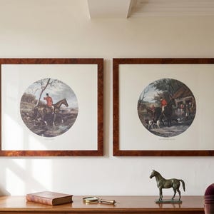 May include: Two framed prints with a hunting scene in a circular design. The frames are a dark wood grain. A bronze horse statue and a magnifying glass sit on a wooden table in front of the prints.