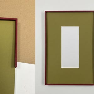 May include: Two framed art pieces. One frame is a deep red with a green interior and a white rectangular opening. The other frame is a deep red with a green interior. The background is a mix of white and beige.