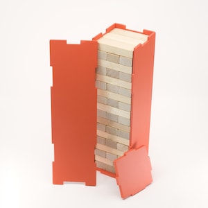May include: A wooden block stacking game with a bright orange frame. The game includes rectangular wooden blocks and an orange container. The container is partially open, revealing the stacked blocks. The game is on a white background.