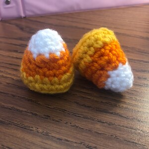 May include: Two crocheted candy corn ornaments in orange, yellow, and white.