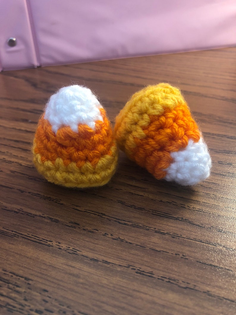 May include: Two crocheted candy corn ornaments in orange, yellow, and white.