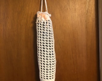 May include: White crocheted mesh bag with a pink drawstring hanging on a wooden door. The bag is empty.