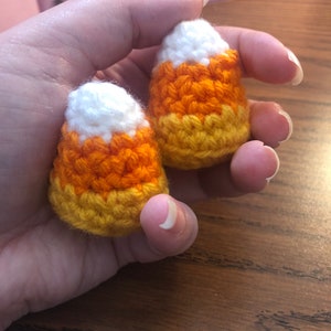 May include: Two crocheted candy corn ornaments in white, orange and yellow.