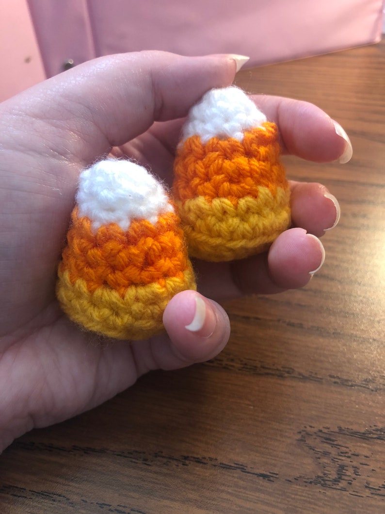 May include: Two crocheted candy corn ornaments in white, orange and yellow.