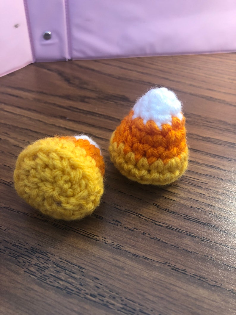 May include: Two crocheted candy corn ornaments, one yellow and orange, the other white, orange, and yellow.