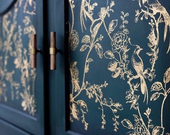 Puede incluir: Puertas de armario de color verde azulado oscuro con diseño floral y de pájaros dorados. El armario tiene dos puertas con tiradores de madera y herrajes dorados. El diseño floral incluye pájaros, flores y hojas. La palabra "KACHA" está en la esquina inferior izquierda.