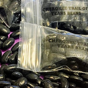 May include: Two clear plastic bags filled with black beans labeled "Cherokee Trail of Tears Beans".