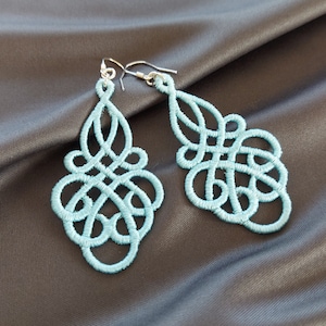 May include: A pair of light blue dangle earrings with a delicate, intricate design. The earrings are made of a woven material and have a silver hook.
