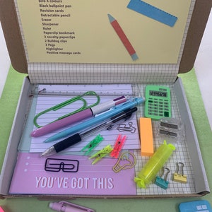 May include: A pink box filled with school supplies for a student going to secondary school. The box includes pens, pencils, a ruler, a calculator, paperclips, a highlighter, and a note that says "You've got this".