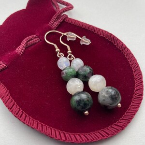 May include: A pair of dangle earrings featuring green, white and grey gemstone beads. The earrings are made with silver-toned metal and have a hook fastening.