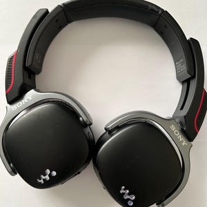 May include: Black Sony headphones with silver accents and red detailing. The headphones have a padded headband and earcups. The Sony logo is visible on the earcups. The headphones have a wireless design.