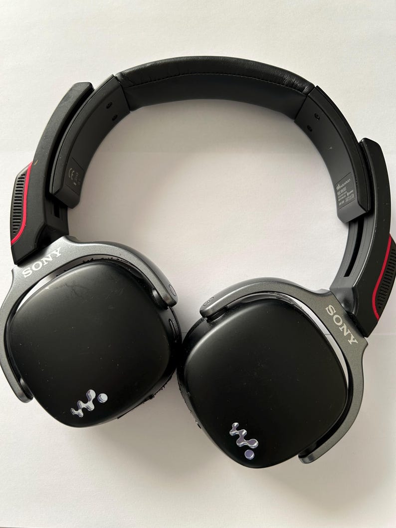 May include: Black Sony headphones with silver accents and red detailing. The headphones have a padded headband and earcups. The Sony logo is visible on the earcups. The headphones have a wireless design.
