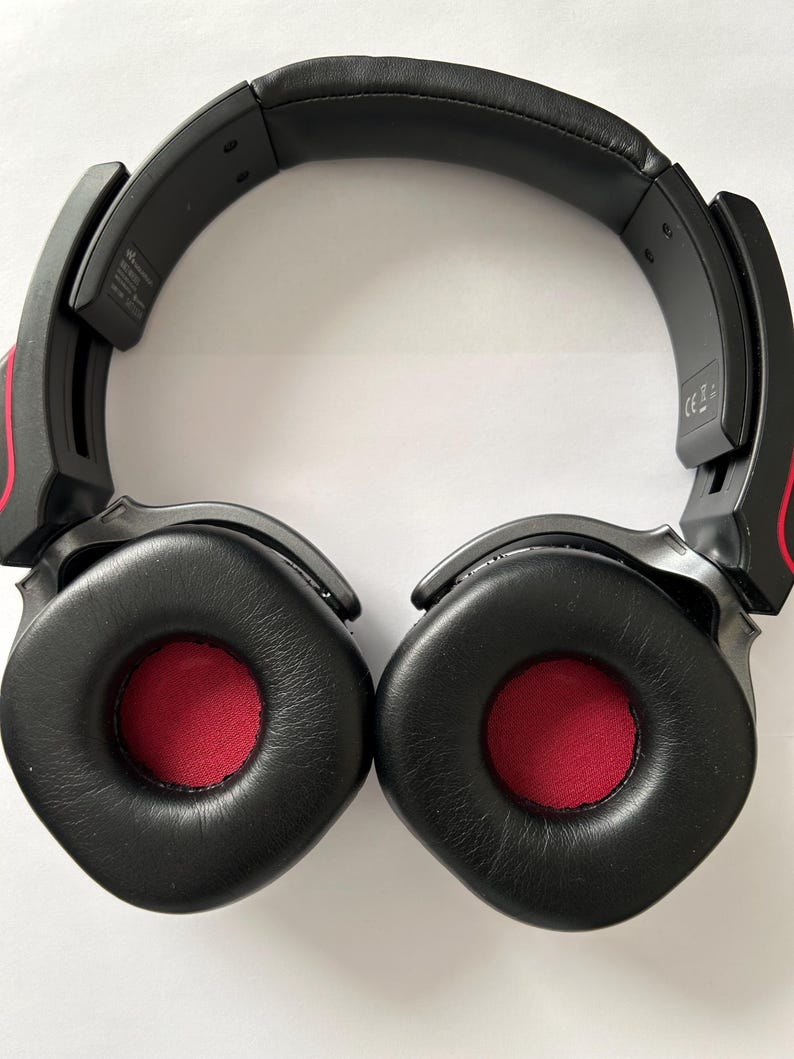 May include: Black over-ear headphones with red accents. The earcups are black with red centers. The headband is black and padded. The headphones are designed for comfort and audio quality.
