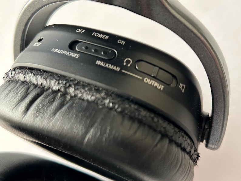 May include: Close-up of black headphones with a silver headband. The control panel has the words "OFF", "POWER", and "ON". There are also controls for "HEADPHONES", "WALKMAN", and "OUTPUT". The ear cushion is black.