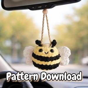 May include: A handmade, crochet bee car charm with black and yellow stripes, white wings, and a smiling face. The bee is suspended from a rearview mirror by a tan cord. The text "Pattern Download" is at the bottom.