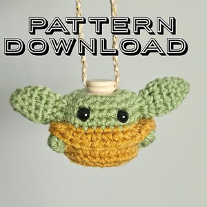 Puede incluir: Una figura de ganchillo de un personaje con orejas grandes, cabeza verde y una prenda amarillo-naranja. La figura tiene ojos negros y está suspendida por una cuerda dorada y blanca. El texto "PATTERN DOWNLOAD" se muestra encima de la figura.