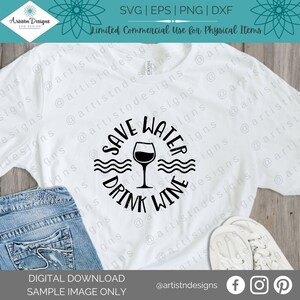 May include: A white t-shirt with a black circle design that says "Save Water Drink Wine" with a wine glass graphic inside the circle. The design is on a white t-shirt with a pair of white sneakers and blue jeans in the background.