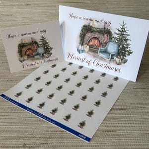 May include: A festive stationery set comprising two Christmas cards and a sheet of stickers. The cards showcase a watercolour illustration of a fireplace, armchair, and Christmas tree, with the text "Have a warm and cosy" and "Merriest of Christmases". The sticker sheet features small Christmas tree designs.