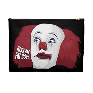 Op de afbeelding: Zwarte etui met ritssluiting met een clowngezicht. De clown heeft een witte huid, rood haar, een rode neus en blauwe oogmake-up. De tekst "KISS ME FAT BOY!" staat aan de linkerkant. De lippen van de clown zijn donkerrood.
