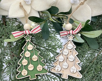 May include: Two wooden Christmas tree ornaments. One is green, the other is natural wood. Each has a star at the top, a red and white striped ribbon, and a jute string for hanging. Names are engraved on the ornaments.