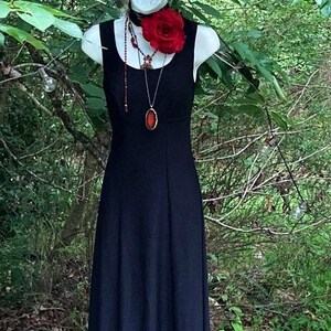 Pu&ograve; includere: Un abito nero senza maniche lungo fino ai piedi con scollo rotondo. L'abito &egrave; arricchito da un girocollo nero con una grande rosa di stoffa rossa e una lunga collana con un ciondolo ovale rosso scuro appeso a una catenina sottile.