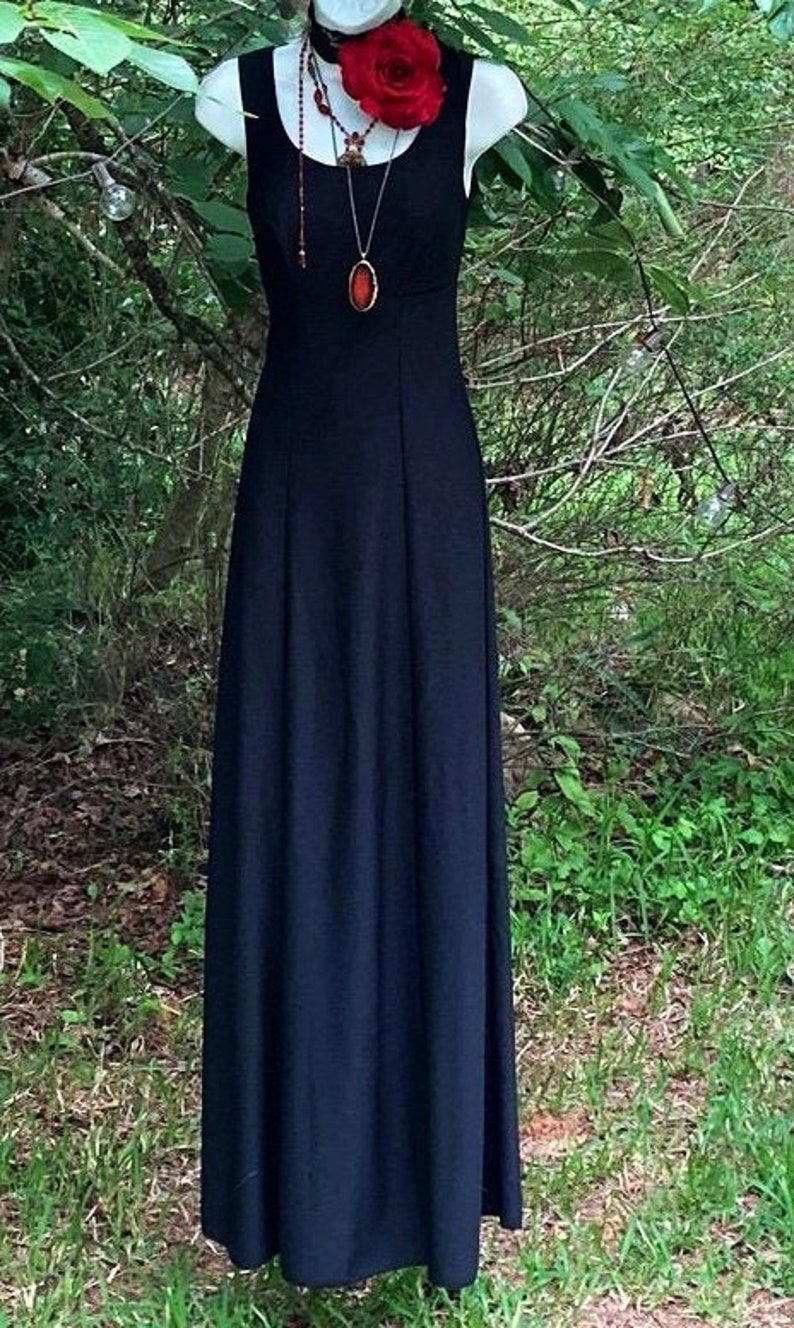 Pu&ograve; includere: Un abito nero senza maniche lungo fino ai piedi con scollo rotondo. L'abito &egrave; arricchito da un girocollo nero con una grande rosa di stoffa rossa e una lunga collana con un ciondolo ovale rosso scuro appeso a una catenina sottile.