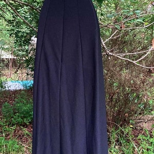 Pu&ograve; includere: Un abito nero senza maniche lungo fino ai piedi con scollo rotondo, un corpetto aderente con cuciture verticali e una gonna lunga e fluida. Il capo &egrave; esposto su un manichino bianco, mostrando un design in tinta unita e una silhouette semplice.
