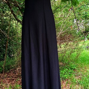 Pu&ograve; includere: Un abito lungo nero senza maniche con scollo quadrato, caratterizzato da un corpetto aderente e una gonna lunga e fluida. L'abito &egrave; completato da un accessorio a forma di rosa rossa per i capelli e una lunga collana con pendente ovale rosso.