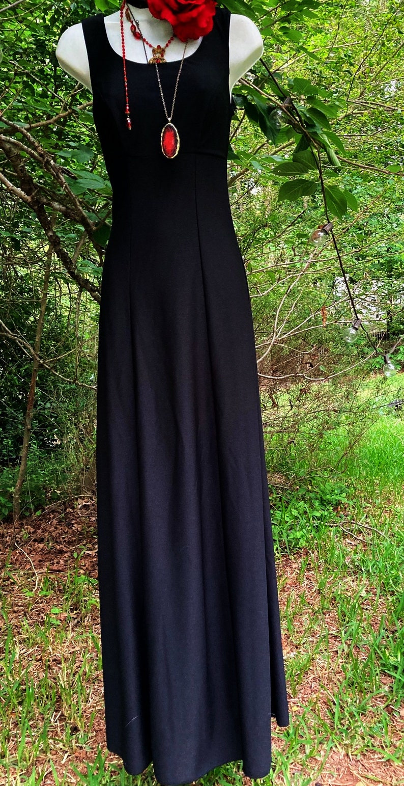 Pu&ograve; includere: Un abito lungo nero senza maniche con scollo quadrato, caratterizzato da un corpetto aderente e una gonna lunga e fluida. L'abito &egrave; completato da un accessorio a forma di rosa rossa per i capelli e una lunga collana con pendente ovale rosso.