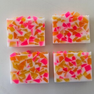 May include: Four bars of handmade soap with a white base and embedded pink and orange pieces. The soap is in a mosaic pattern.