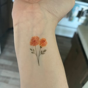 May include: A temporary tattoo with two orange flowers and green stems.