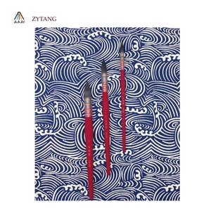 May include: Three red handled paint brushes with black bristles, arranged vertically on a blue and white patterned fabric background.