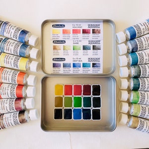 May include: A collection of Schmincke Horadam Aquarell watercolor paints. The set includes tubes of paint and a palette of dried watercolors in a metal tin. The tubes are labeled with the brand name and color information. The colors range from blues and greens to reds and yellows.