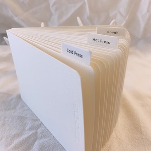 May include: A white, fan-shaped stack of paper with three tabs labeled "Rough", "Hot Press", and "Cold Press".
