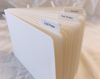 May include: A white, fan-shaped stack of paper with three tabs labeled "Rough", "Hot Press", and "Cold Press".