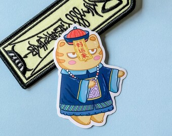 May include: A cartoon sticker of a yellow cat wearing a blue and purple robe with a red hat and a red and white sign that says "好运来" in Chinese characters. The cat has a serious expression on its face.