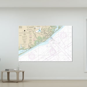 May include: A nautical chart of an area with land, water, and navigational markers. The chart is displayed on a wall, with a gray chair and small table in front of it. The chart has text and lines.