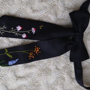 May include: A black bow tie with embroidered flowers in shades of pink, blue, orange, and green.