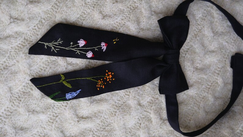 May include: A black bow tie with embroidered flowers in shades of pink, blue, orange, and green.
