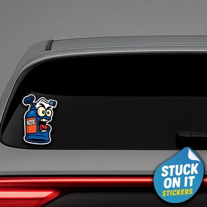 May include: A blue and orange cartoon sticker of a NOS tank with a face, applied to a car window. The sticker has a white outline and the word "NOS" is visible. The sticker is next to a blue sticker that says "STUCK ON IT STICKERS".