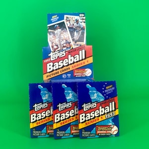 May include: Stacked boxes of 1993 Topps Major League Baseball Series 1 trading cards. The boxes are blue, red, and yellow with images of baseball players and the Topps logo. The background is a solid green.