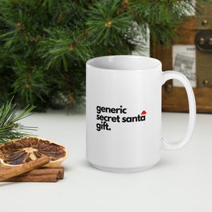 May include: White ceramic coffee mug with a black graphic that says "generic secret santa gift." The graphic also includes a small red Santa hat.