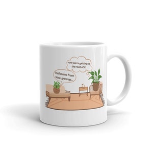 May include: White ceramic mug with a brown cartoon illustration of a living room with two potted plants. The text on the mug reads "now we're getting to the root of it. it all stems from how i grew up..."