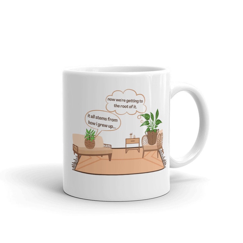 May include: White ceramic mug with a brown cartoon illustration of a living room with two potted plants. The text on the mug reads "now we're getting to the root of it. it all stems from how i grew up..."