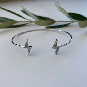 May include: Silver bangle bracelet with two lightning bolt charms, each set with clear cubic zirconia stones.