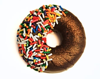 May include: A chocolate donut with sprinkles. The donut is covered in chocolate frosting and has a dusting of gold glitter.